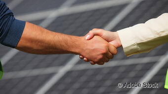 Das Bild zeigt zwei Menschen, die sich die Hand geben und im Hintergrund ist eine Photovoltaik Analge zu sehen. Das Bild zeigt zwei Menschen, die sich die Hand geben und im Hintergrund ist eine Photovoltaik Analge zu sehen.